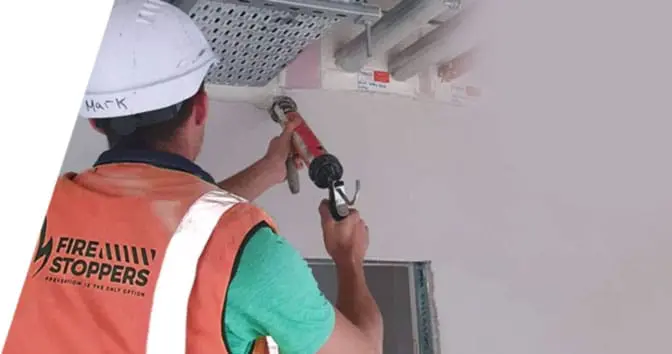 engineer applying an intumescent coating to a strucutral steel beam. Enginner is dressed in hi-vis jacket and a white safety hat