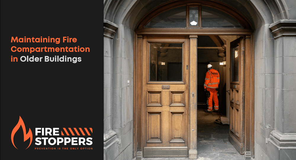 A photo of an older building in Ireland with fire compartmentation. There is a wooden door with a window at eye level. The door is slightly ajar, revealing a dark hallway with a few doors. The walls and floors are made of stone. The lighting is low. A construction worker wearing orange hi vis and his back to the camera